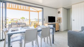 Una sala de estar moderna con comedor, puertas correderas de vidrio que dan a un balcón, televisor de pantalla plana y un reloj en la pared.