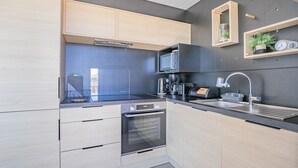 Una cocina moderna con armarios de madera clara, encimera negra, horno empotrado, microondas, cafetera y un lavabo con grifo.