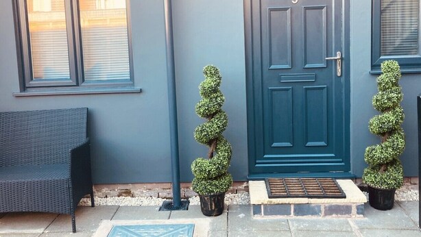 A front door with a number, a bench, and two potted topiary plants.