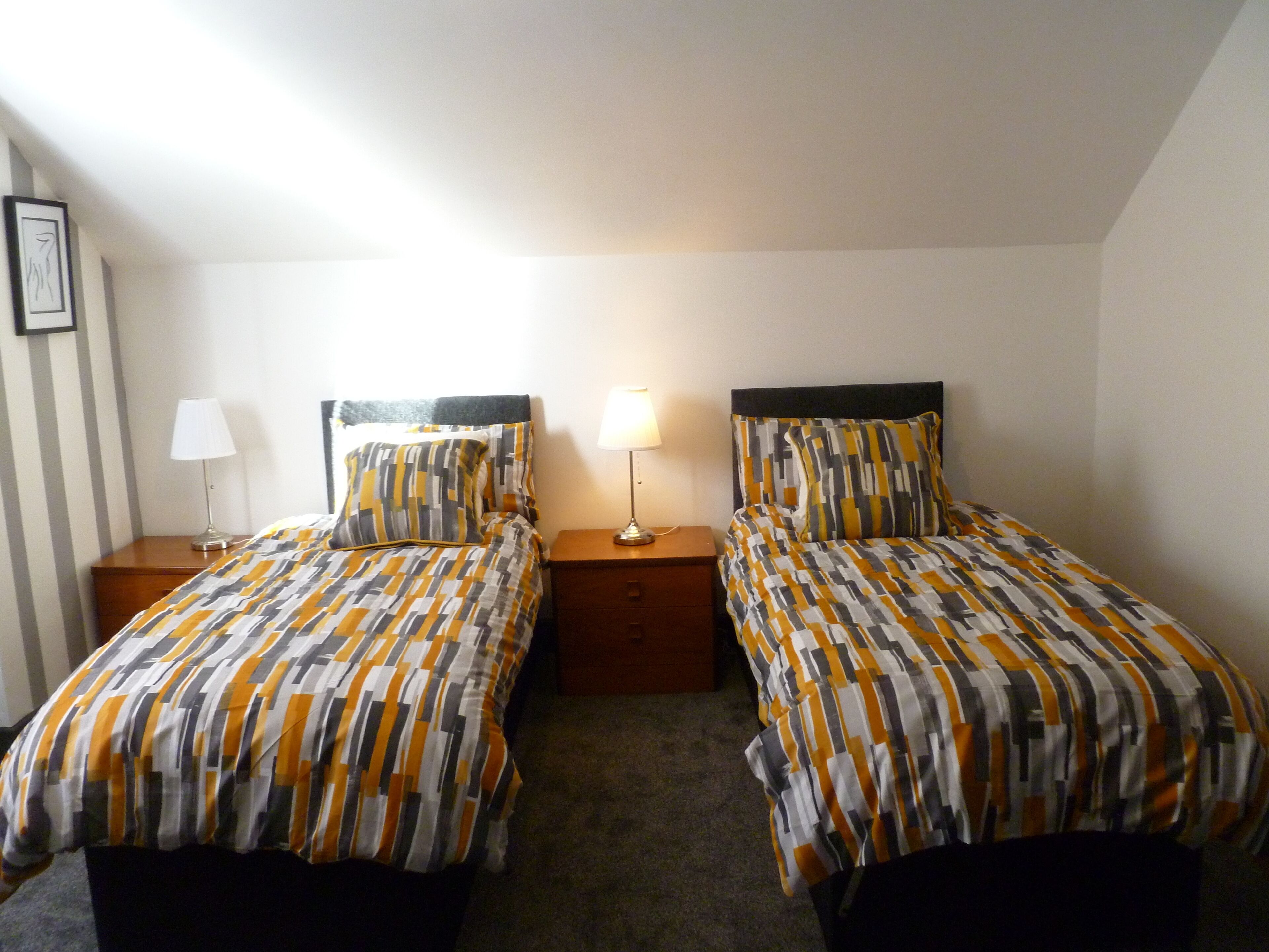 Camera doppia con due letti, ognuno con una coperta fantasia e cuscini coordinati, affiancati da comodini con lampade.