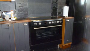 A kitchen with a black stove, oven, and black refrigerator. There is a wooden countertop and grey cabinets.