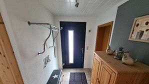 A hallway with a bench, a coat rack, a wooden cabinet, and a door with a window.