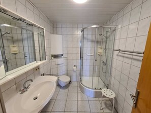 Een moderne badkamer met een douchecabine van glas, een wastafel, toilet en spiegel.