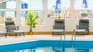 Un área de piscina interior con agua azul cristalina, rodeada de ventanales que dan a una terraza de madera y plantas en macetas.
