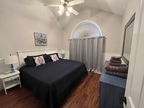 Un dormitorio con cama, mesita de noche, lámpara y ventana con cortinas.