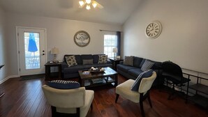 Een woonkamer met een plafondventilator, twee banken, een salontafel en een deur met een raam.