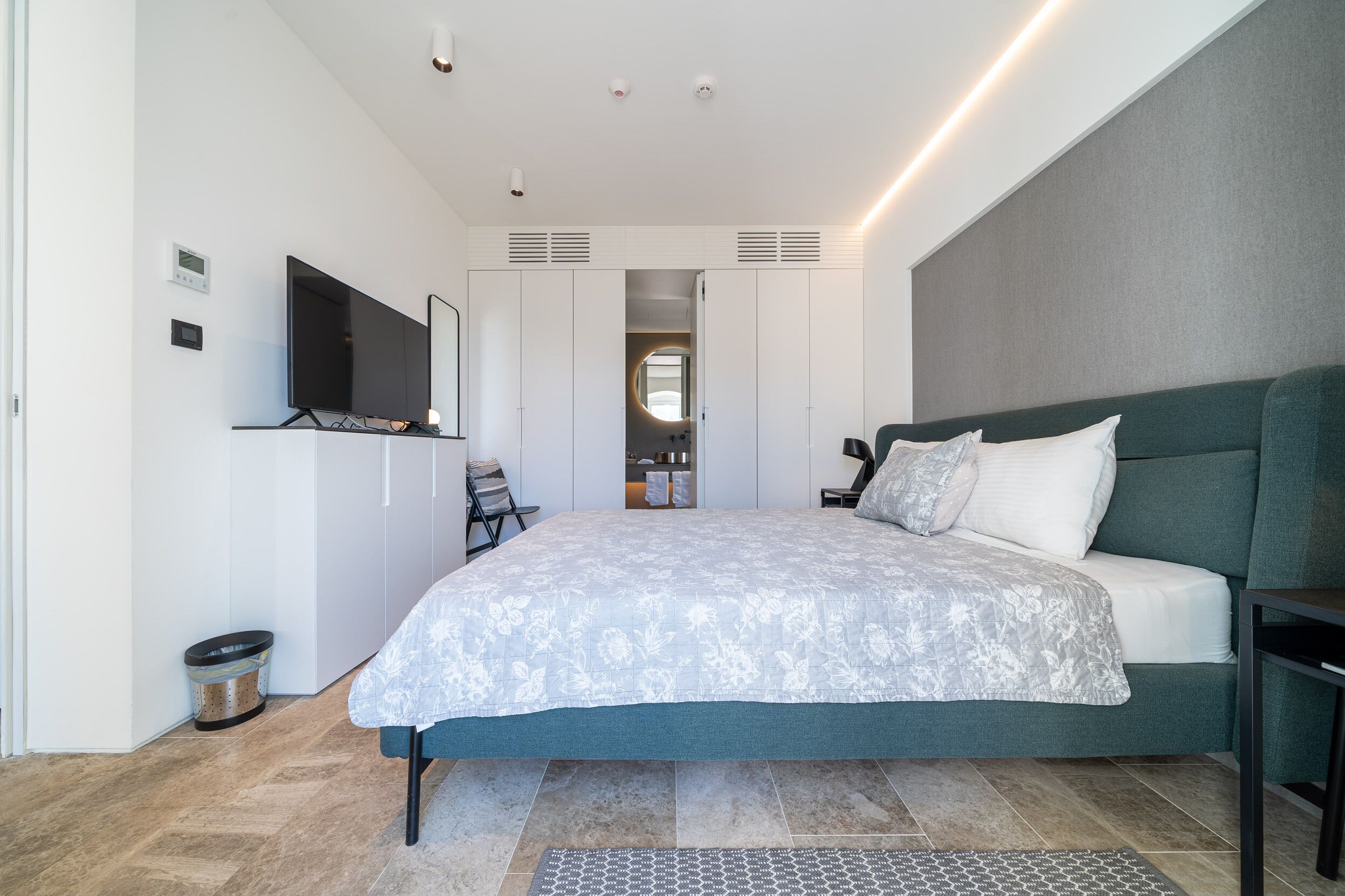 A modern bedroom with a large bed, a TV mounted on the wall, and a walk-in closet.