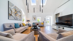 Een ruime woonkamer met een grote televisie, comfortabele zithoek, een salontafel en kunstwerken aan de wanden.