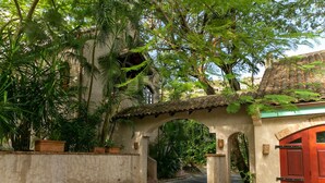 A pathway leading to a building with a red door, surrounded by lush greenery and an archway. - One Bedroom Cottage on Peter Bay Beach (St John)