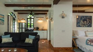 A cozy living area with a dark sofa, a small round table, and a bed with a decorative pillow. - One Bedroom Cottage on Peter Bay Beach (St John)