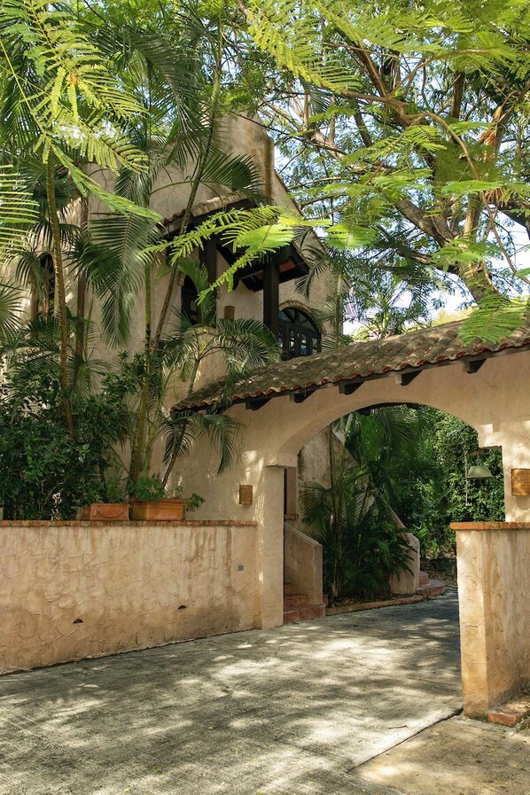 A covered walkway with a rustic stone archway, surrounded by lush greenery and palm trees. - One Bedroom Cottage on Peter Bay Beach (St John)