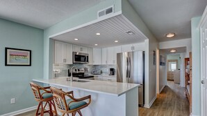 Una cocina moderna con armarios blancos, electrodomésticos de acero inoxidable y una isla central con taburetes de bar.
