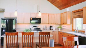 Une cuisine moderne avec des armoires en bois, un réfrigérateur noir, un four à micro-ondes et une cuisinière. On y trouve deux chaises en bois et une table au centre.