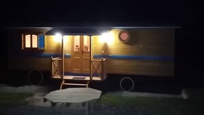 En liten, envåningsbyggnad med en veranda och en dörr, upplyst av utomhusbelysning.