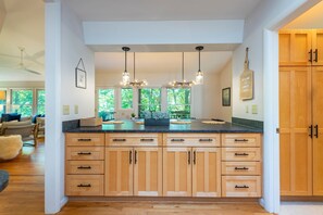 A modern kitchen with wooden cabinets, a granite countertop, pendant lights, and a view of the outdoors.