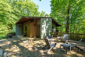 Un chalet rustique doté d’un patio en pierre, de meubles de jardin et d’une terrasse en bois offrant une vue sur une forêt.
