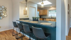 Uma cozinha moderna com ilha central, banquetas e iluminação pendente.