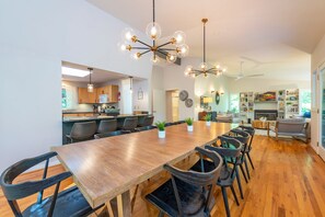 Een moderne eetruimte met een lange houten tafel en zwarte stoelen, een keuken met houten kastjes en een woonkamer met een bank en een open haard.
