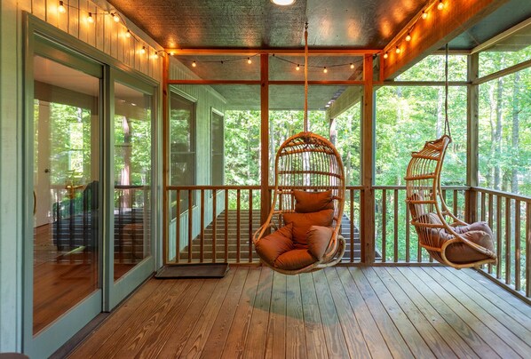 Lower-level screened-in porch with ceiling fan, hanging chairs, and a variety of seating
