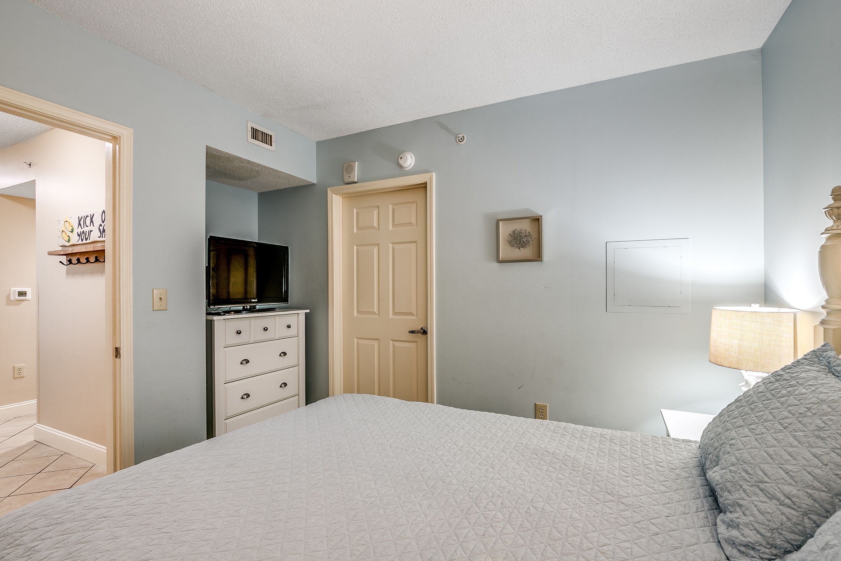 Een slaapkamer met een bed, een dressoir, een televisie en een deur.