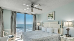 A bedroom with a large bed, a ceiling fan, a view of the ocean, and a white nightstand with a lamp. - 🌟Large Oceanfront~Lazy River~Awesome Amenities~ Caribbean Resort 503🌟 (Myrtle Beach)