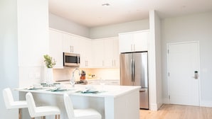 Una cocina moderna con armarios blancos, electrodomésticos de acero inoxidable y una isla central con taburetes de bar.