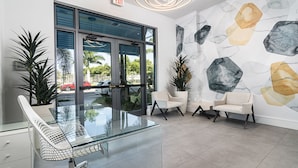 Un vestíbulo moderno con una mesa de cristal, dos sillones blancos y una pared de mármol.