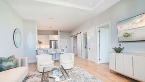 Una sala de estar moderna con un sofá, dos sillones blancos, una mesa de centro y un televisor montado en la pared.