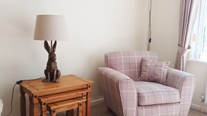 Une pièce chaleureuse avec une petite table d’appoint en bois, une lampe ornée d’une figurine de lapin et un canapé à carreaux.