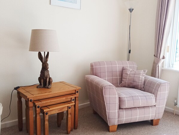 A cozy room with a wooden side table, a lamp with a rabbit figurine, and a plaid sofa.
