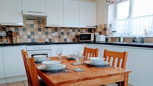 Une cuisine moderne avec des meubles blancs, un pare-feu en carrelage et une table à manger pour quatre personnes, accompagnée de chaises.