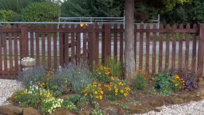 Un jardin avec une clôture en bois, diverses plantes à fleurs et un arbre.