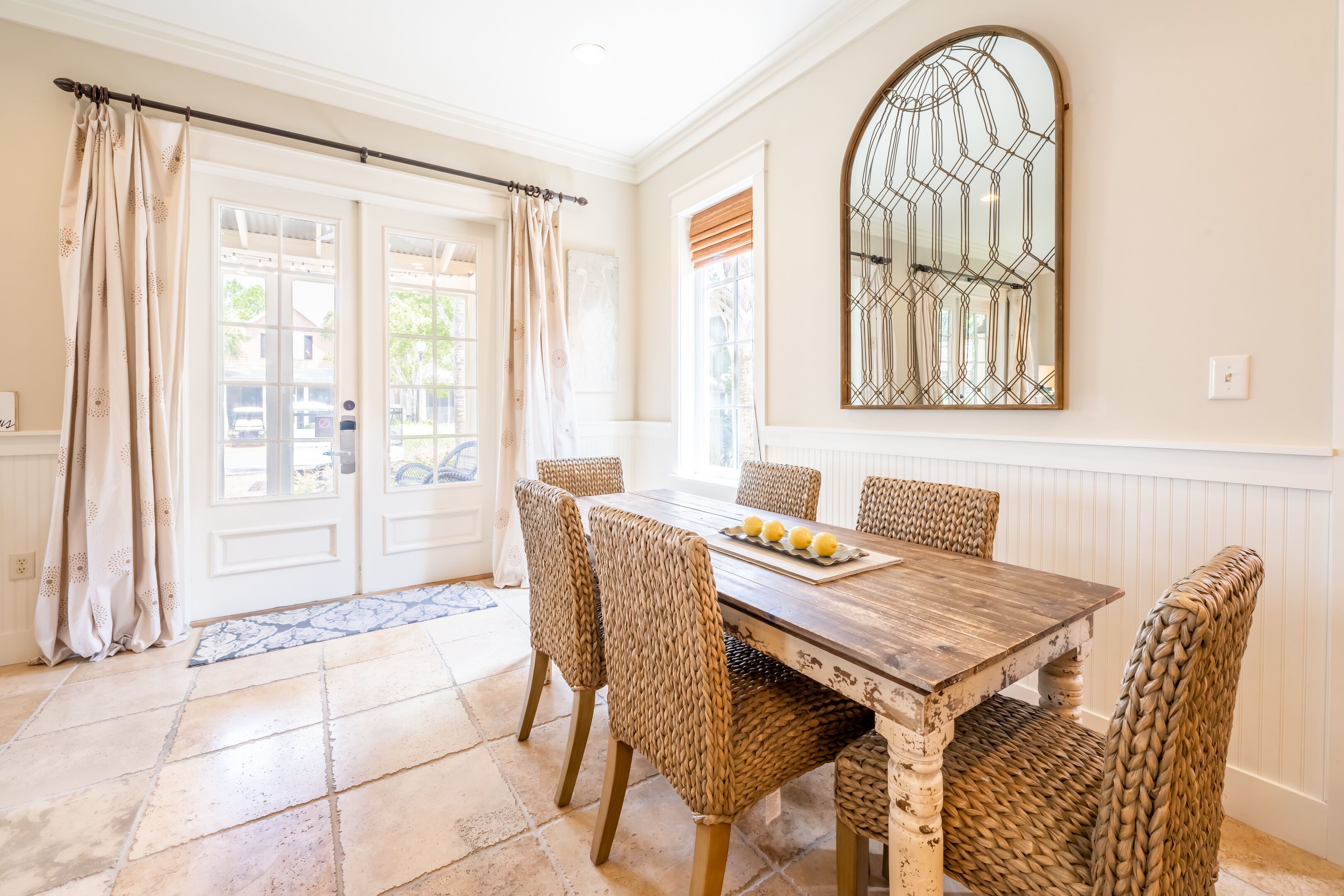A dining area with a wooden table, woven chairs, and a decorative mirror.