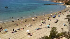 A beach with people sunbathing and swimming, a boat in the water, and buildings in the background. - Very nice apartment in 1st line of golf (VC)
