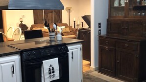 Uma cozinha com fogão preto, armários brancos, um aparador de madeira com portas de vidro e uma área de jantar com sofá marrom e mesa de centro.