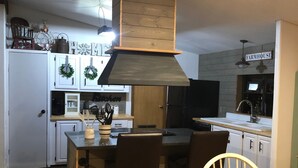 Uma cozinha com ilha central, armários brancos e uma placa rústica.
