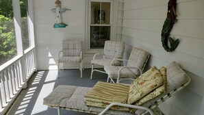 A covered porch with a white metal chair, a cushioned bench, and a window. - Pine Island Retreat - 3BR's, 1st & 2nd level porches NO LINENS PROVIDED (Chincoteague)