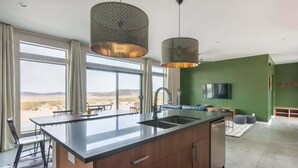A modern kitchen with a central island, large windows, and a view of the outdoors. - Estrella Perdida by Homestead Modern (Joshua Tree)