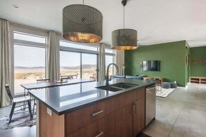 A modern kitchen with a large island, a dining area with a view, and a living space with a TV.