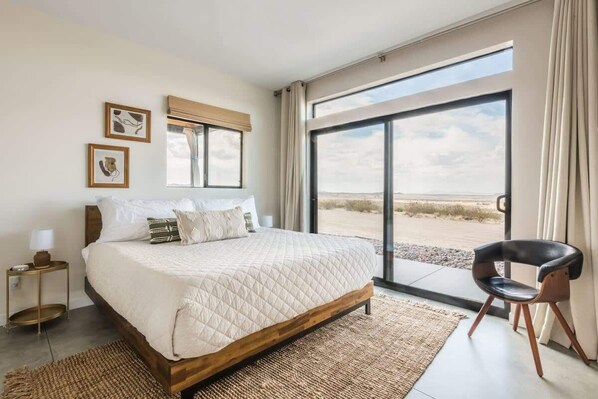 A bedroom with a large bed, a view of the beach, and a chair by the window.