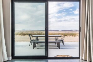 A sliding glass door leading to an outdoor patio with a table and chairs, a view of a desert landscape, and a clear sky.