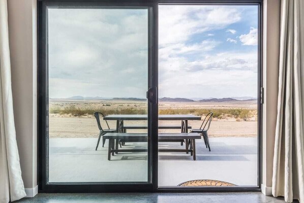 A sliding glass door leading to an outdoor patio with a table and chairs, a view of a desert landscape, and a clear sky.