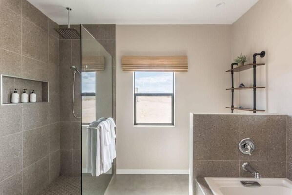 Un baño moderno con ducha, un ventanal grande y un estante empotrado con artículos de aseo.