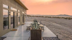 A modern building with large windows, a patio area with a plant, and a view of distant mountains. - Estrella Perdida by Homestead Modern (Joshua Tree)