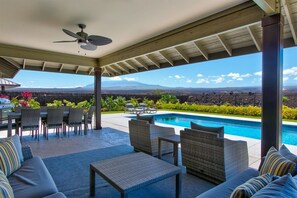 A covered outdoor area with a pool, seating, and a view of distant mountains. - Luxury Home w/Pool + Spa | Sleeps 10 | Waikoloa Resort (Waikoloa)
