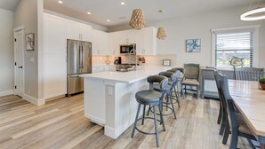 A modern kitchen with white cabinetry, a stainless steel refrigerator, a central island with bar stools, and pendant lighting. - Luxury Home w/Pool + Spa | Sleeps 10 | Waikoloa Resort (Waikoloa)