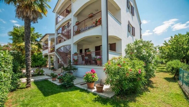 Un edificio de varios pisos con balcones, un jardín con plantas en macetas y un cielo despejado.