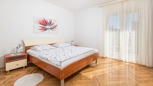 Un dormitorio con una cama de madera, cortinas blancas, una mesita de noche con una lámpara y una obra de arte en la pared.