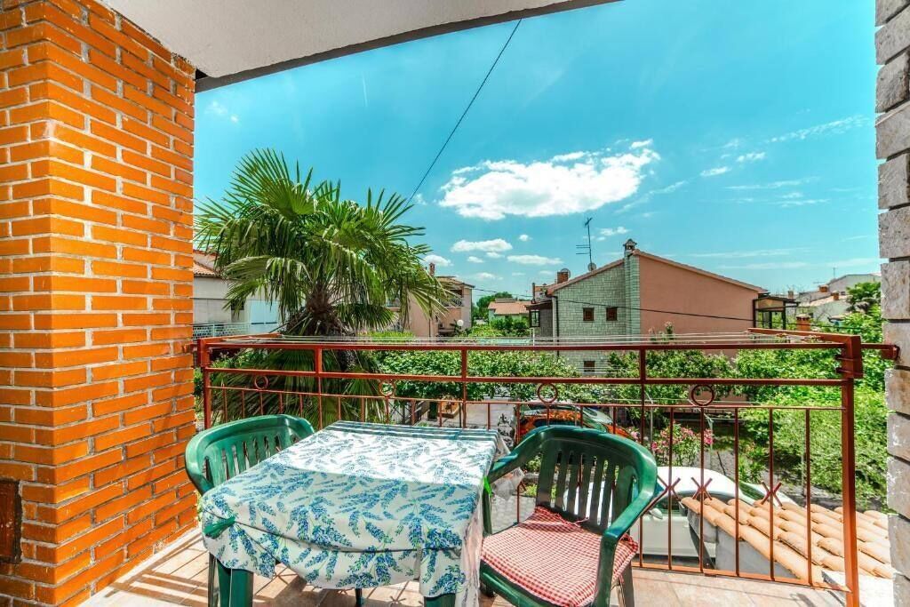 En balkon med et bord og stole, et palmetræ og udsigt til nabohuse.