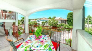 Un balcón con mesa y sillas, plantas en macetas y vistas a casas y follaje.